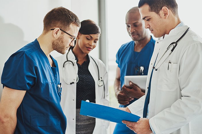 medical doctors and nurse practitioners discuss paperwork in a hallway